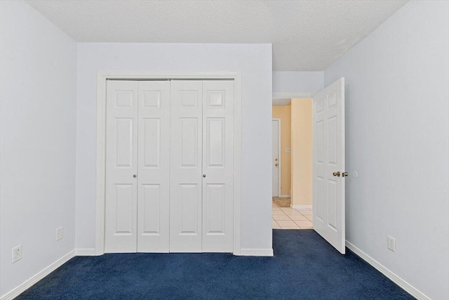unfurnished bedroom featuring dark carpet, a closet, a textured ceiling, and baseboards