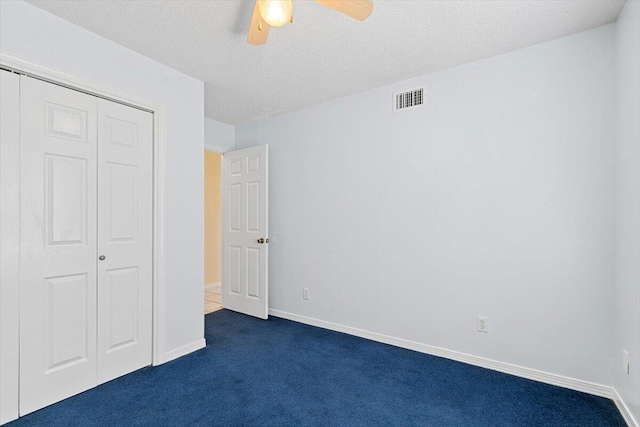 unfurnished bedroom with dark carpet, a closet, a ceiling fan, baseboards, and a textured ceiling