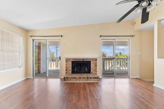unfurnished living room with wood finished floors, a ceiling fan, and a brick fireplace