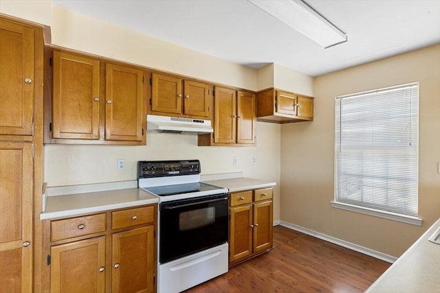 kitchen featuring range with electric stovetop, under cabinet range hood, brown cabinets, light countertops, and dark wood finished floors