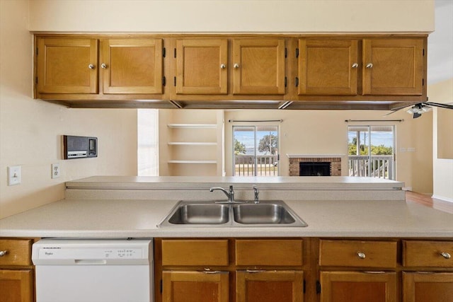 kitchen with dishwasher, a sink, light countertops, brown cabinets, and a brick fireplace