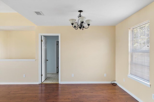 unfurnished room featuring a chandelier, wood finished floors, and baseboards