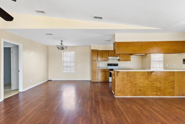 kitchen with electric range oven, brown cabinets, under cabinet range hood, light countertops, and dark wood-type flooring