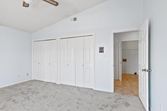 unfurnished bedroom featuring lofted ceiling, multiple closets, carpet flooring, ceiling fan, and tile patterned flooring