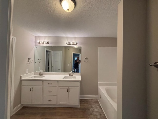 bathroom with a textured ceiling, a bath, double vanity, wood finished floors, and baseboards