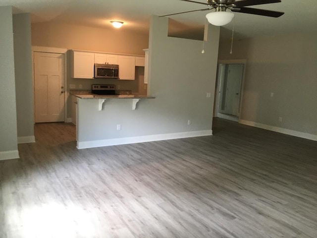 kitchen featuring appliances with stainless steel finishes, a ceiling fan, white cabinetry, a kitchen bar, and wood finished floors