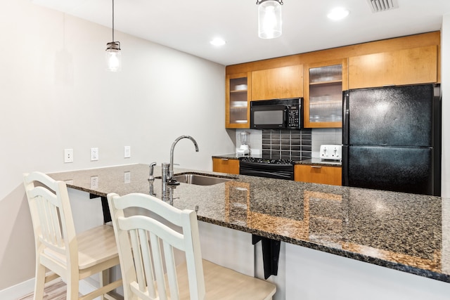 kitchen with black appliances, a sink, brown cabinets, dark stone countertops, and glass insert cabinets