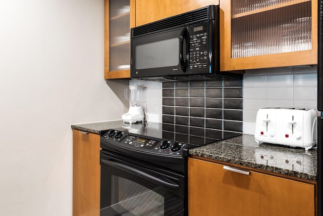 kitchen with black appliances, brown cabinetry, backsplash, glass insert cabinets, and dark stone counters