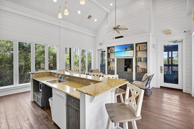 kitchen with a sink, high vaulted ceiling, dark wood finished floors, a kitchen bar, and a center island with sink