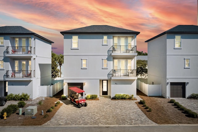 view of front of property featuring a balcony, french doors, fence, and a garage