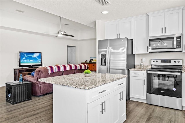 3163 Haskell Langley Rd, Crestview, FL 32539 - kitchen with appliances with stainless steel finishes, wood finished floors, open floor plan, white cabinetry, and a textured ceiling