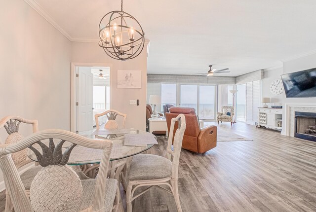 8601 Surf Dr Unit 2W, Panama City Beach, FL 32408 - dining room featuring ceiling fan, a chandelier, light wood-style floors, crown molding, and a tiled fireplace