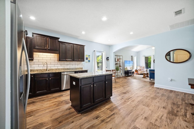 kitchen featuring appliances with stainless steel finishes, arched walkways, plenty of natural light, wood finished floors, and recessed lighting