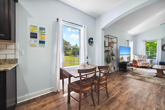 dining space with dark wood finished floors, arched walkways, lofted ceiling, and baseboards