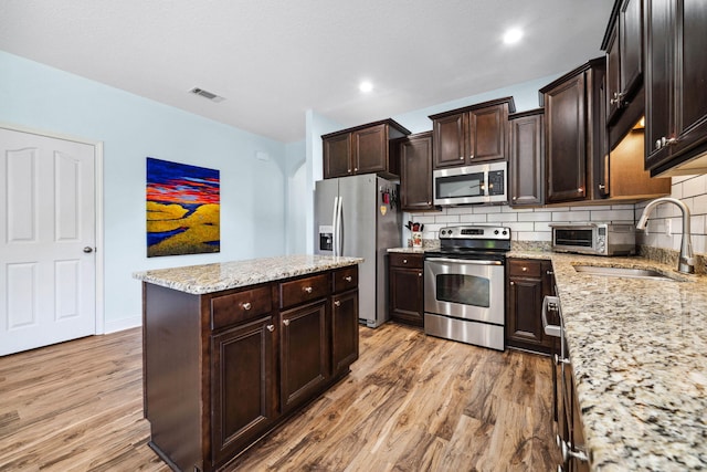 kitchen with appliances with stainless steel finishes, a center island, a sink, light wood-style floors, and tasteful backsplash