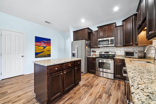 kitchen featuring stainless steel appliances, light wood finished floors, a center island, decorative backsplash, and a sink