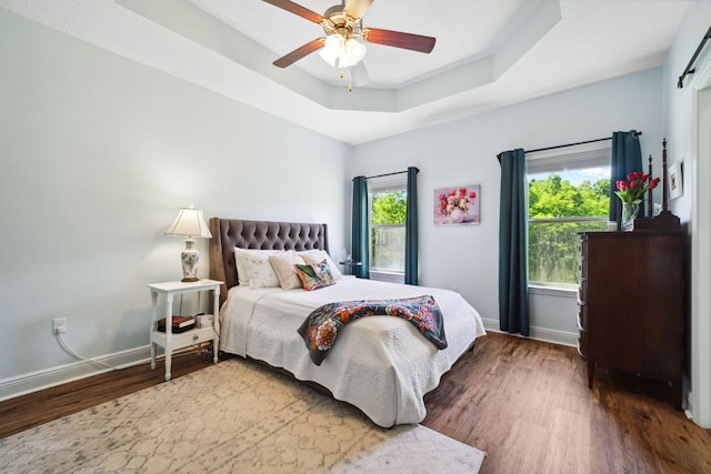 bedroom featuring wood finished floors, baseboards, a raised ceiling, and ceiling fan