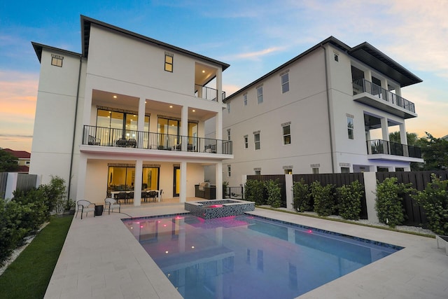 336 S Holiday Rd, Destin, FL 32550 - back of property at dusk with a balcony, stucco siding, a patio area, and a pool with connected hot tub