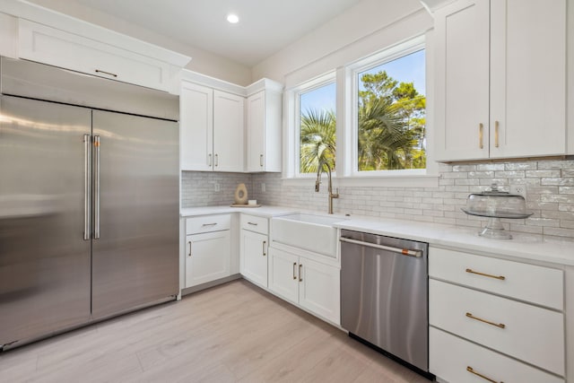 55 May Dr, Santa Rosa Beach, FL 32459 - kitchen featuring appliances with stainless steel finishes, a sink, decorative backsplash, white cabinetry, and light wood finished floors