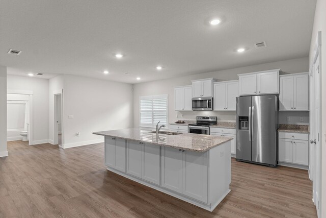 608 Champ Trl, Crestview, FL 32539 - kitchen with stainless steel appliances, a sink, white cabinets, wood finished floors, and an island with sink