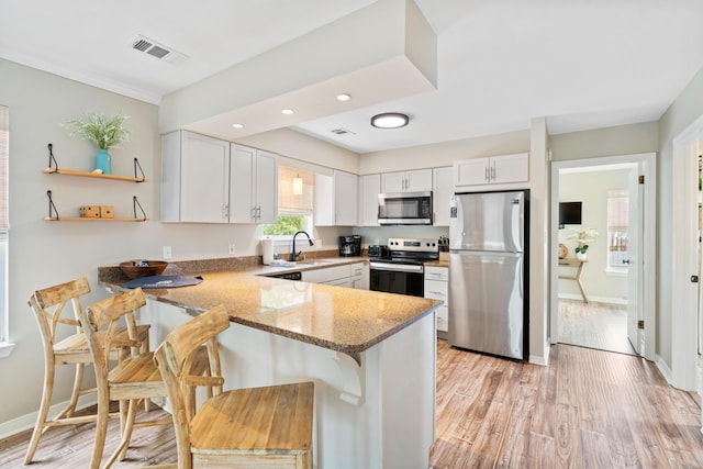 4508 Luke Ave, Destin, FL 32541 - kitchen featuring appliances with stainless steel finishes, a peninsula, light stone counters, a sink, and light wood-type flooring