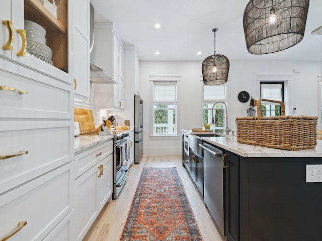 241 N 7th St, Santa Rosa Beach, FL 32459 - kitchen with stainless steel appliances, wall chimney exhaust hood, white cabinetry, a kitchen island with sink, and a sink