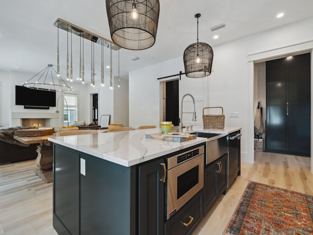 241 N 7th St, Santa Rosa Beach, FL 32459 - kitchen featuring stainless steel appliances, a barn door, an island with sink, light wood-style floors, and hanging light fixtures