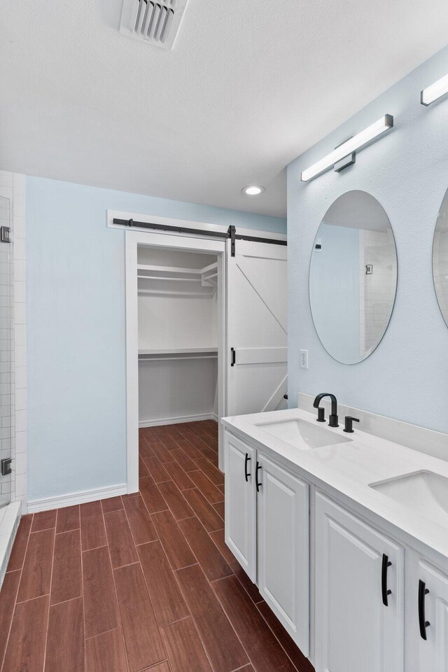 276 Sandy Cay Dr, Miramar Beach, FL 32550 - bathroom with double vanity, a walk in closet, wood finished floors, a tile shower, and a textured ceiling
