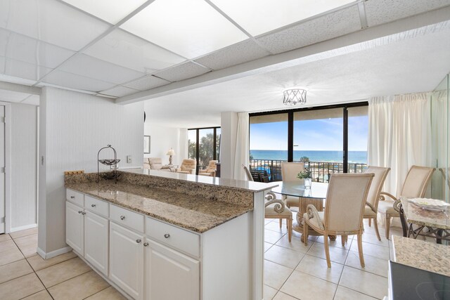 11483 Front Beach Rd Unit 202, Panama City Beach, FL 32407 - kitchen featuring light tile patterned flooring, a peninsula, white cabinets, light stone counters, and a paneled ceiling