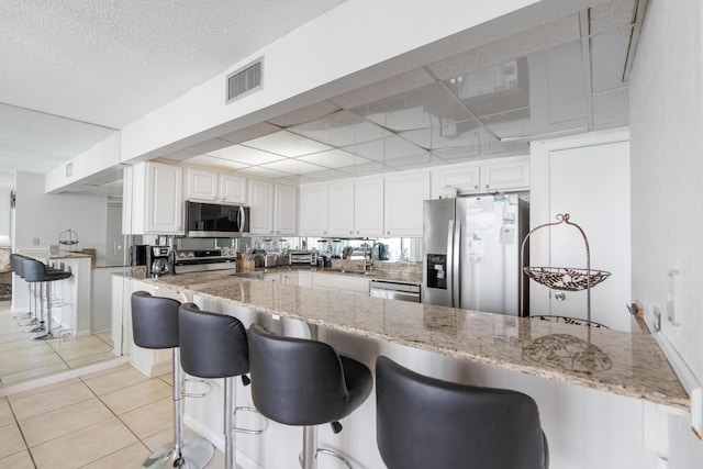 11483 Front Beach Rd Unit 202, Panama City Beach, FL 32407 - kitchen featuring appliances with stainless steel finishes, a peninsula, light stone countertops, white cabinets, and a breakfast bar