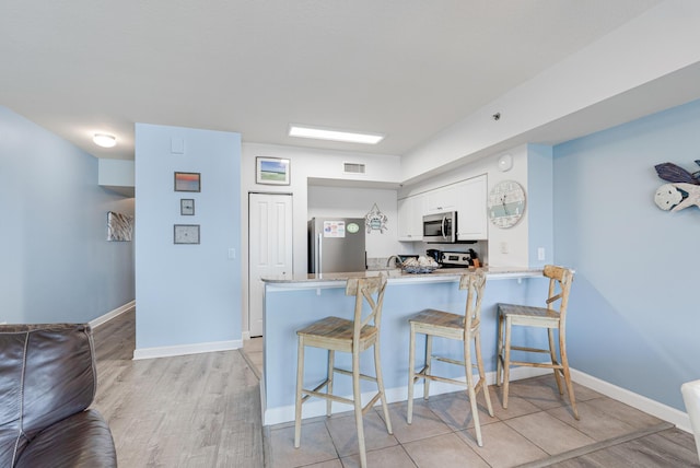 9900 S Thomas Dr Unit 2226, Panama City Beach, FL 32408 - kitchen featuring appliances with stainless steel finishes, a peninsula, a kitchen bar, white cabinets, and baseboards
