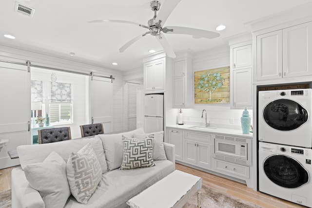 29 Tidal Bridge Way, Watersound, FL 32461 - laundry area featuring stacked washing machine and dryer, a sink, a barn door, light wood-style flooring, and a ceiling fan
