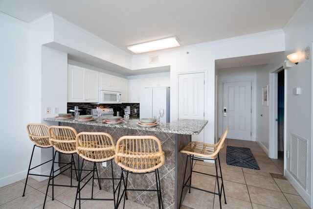 17757 Front Beach Rd Unit 1205C, Panama City Beach, FL 32413 - kitchen featuring white appliances, a peninsula, decorative backsplash, ornamental molding, and a breakfast bar