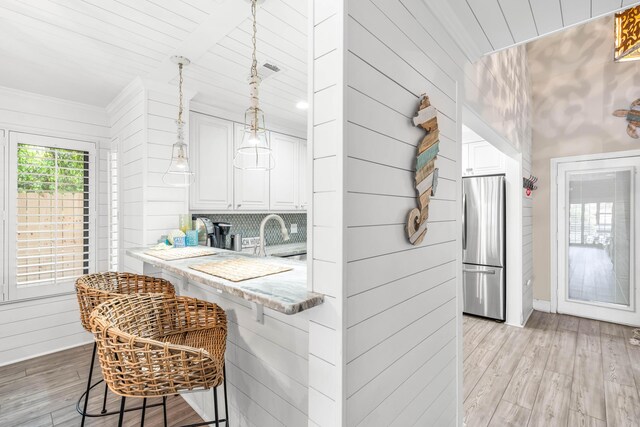 5209 Beachwalk Dr, Miramar Beach, FL 32550 - kitchen with freestanding refrigerator, light wood-style floors, a sink, white cabinetry, and wood walls