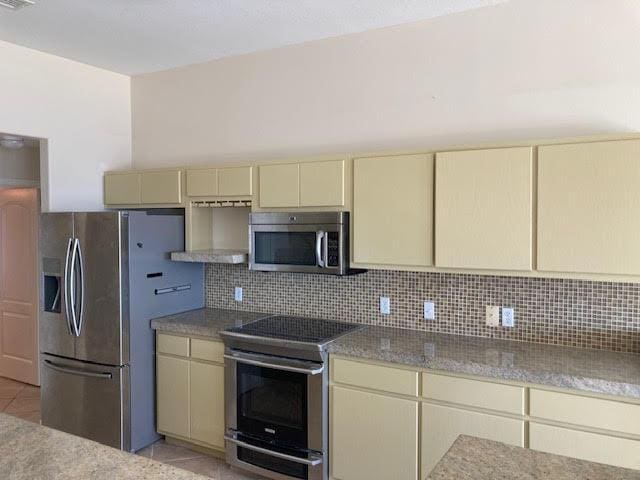6735 Tidewater Dr, Navarre, FL 32566 - kitchen with cream cabinetry, appliances with stainless steel finishes, light tile patterned flooring, and decorative backsplash