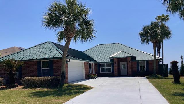 6735 Tidewater Dr, Navarre, FL 32566 - ranch-style home featuring an attached garage, brick siding, concrete driveway, a front yard, and a standing seam roof