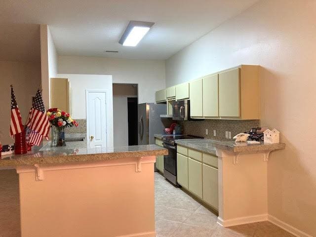 6735 Tidewater Dr, Navarre, FL 32566 - kitchen featuring electric range, a peninsula, a breakfast bar, tasteful backsplash, and freestanding refrigerator