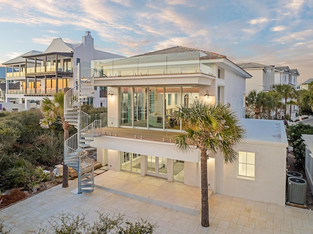 40 Jasmine Cir, Santa Rosa Beach, FL 32459 - back of house at dusk featuring stairs, stucco siding, a patio, central AC unit, and a sunroom