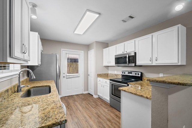1014 Airport Rd Unit 155, Destin, FL 32541 - kitchen featuring appliances with stainless steel finishes, a sink, light stone countertops, white cabinetry, and light wood-style floors