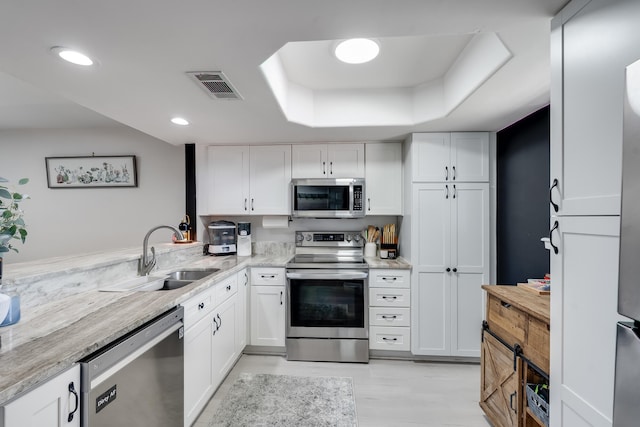 16 Court Dr, Destin, FL 32541 - kitchen with appliances with stainless steel finishes, white cabinetry, a sink, a raised ceiling, and light stone counters