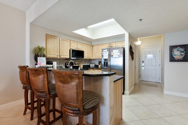 112 Seascape Dr Unit 1807, Miramar Beach, FL 32550 - kitchen with appliances with stainless steel finishes, light brown cabinets, dark countertops, light tile patterned floors, and a peninsula