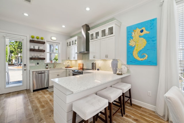 300 Cassine Garden Cir, Santa Rosa Beach, FL 32459 - kitchen with appliances with stainless steel finishes, wall chimney range hood, a peninsula, light wood-type flooring, and decorative backsplash
