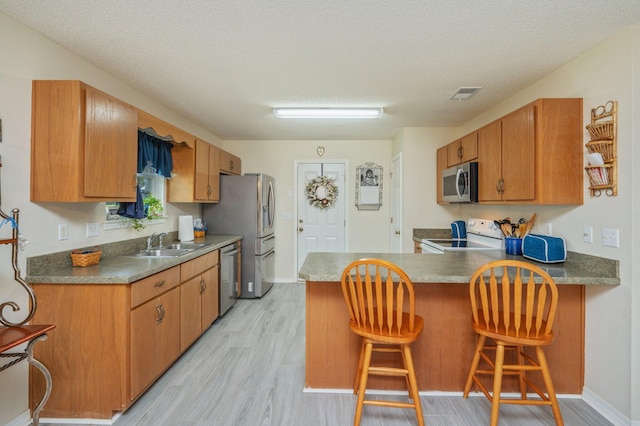 642 Alysheba Dr, Crestview, FL 32539 - kitchen featuring appliances with stainless steel finishes, light wood finished floors, a sink, brown cabinets, and a peninsula