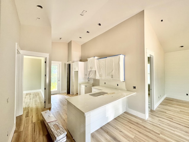 298 S 2nd St, Santa Rosa Beach, FL 32459 - kitchen with high vaulted ceiling, light wood-style flooring, a peninsula, baseboards, and white cabinetry