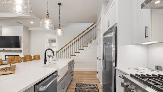 51 W Okeechobee, Santa Rosa Beach, FL 32459 - kitchen with appliances with stainless steel finishes, wall chimney range hood, light wood-type flooring, a sink, and hanging light fixtures