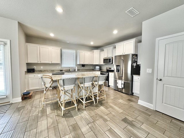 74 Tranquility Ln, Santa Rosa Beach, FL 32459 - kitchen with stainless steel appliances, wood tiled floors, a kitchen island, white cabinetry, and recessed lighting