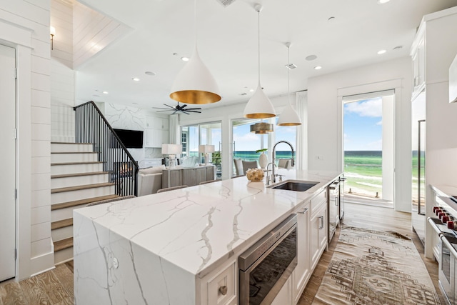 323 Pompano St, Inlet Beach, FL 32461 - kitchen with a sink, appliances with stainless steel finishes, white cabinets, light wood-style flooring, and a center island with sink