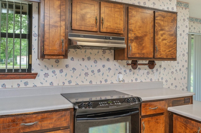 1131 Stanley Ln, Baker, FL 32531 - kitchen with black range with electric cooktop, under cabinet range hood, wallpapered walls, light countertops, and brown cabinets