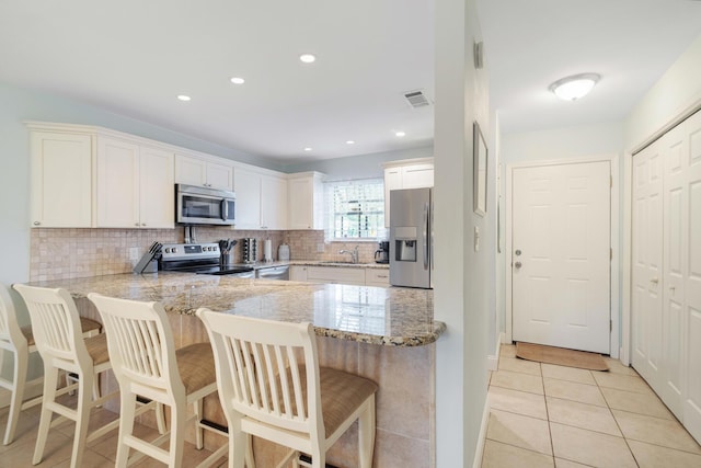 25 Misty Cv Unit 115, Miramar Beach, FL 32550 - kitchen featuring appliances with stainless steel finishes, a sink, a peninsula, decorative backsplash, and white cabinetry