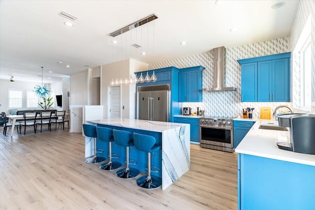 8169 White Sands Blvd, Navarre, FL 32566 - kitchen with high quality appliances, wall chimney exhaust hood, blue cabinetry, a sink, and recessed lighting